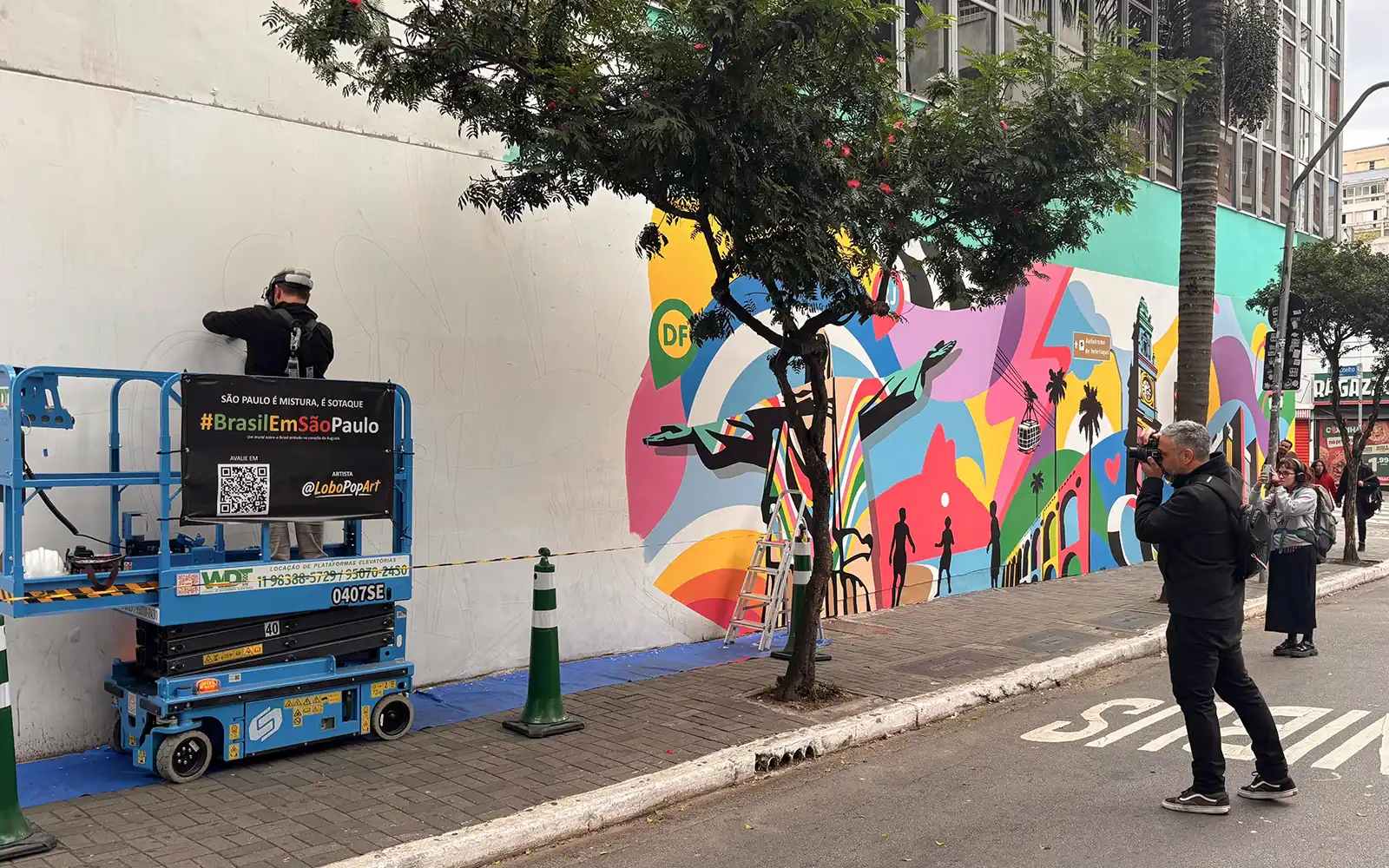 Lobo Pop Art pinta o mural Brasil em São Paulo enquanto visitantes fotografam a obra na Rua Augusta