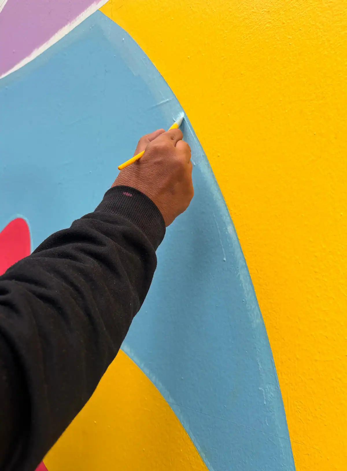 Pincel aplica tinta azul-clara em um detalhe colorido do mural na Rua Augusta