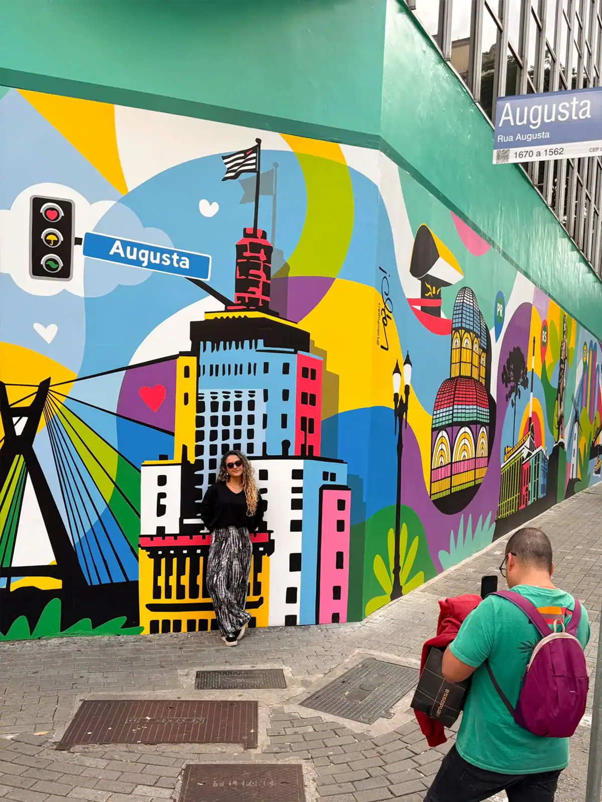 Visitante posa diante do mural na Rua Augusta enquanto outra pessoa faz a fotografia
